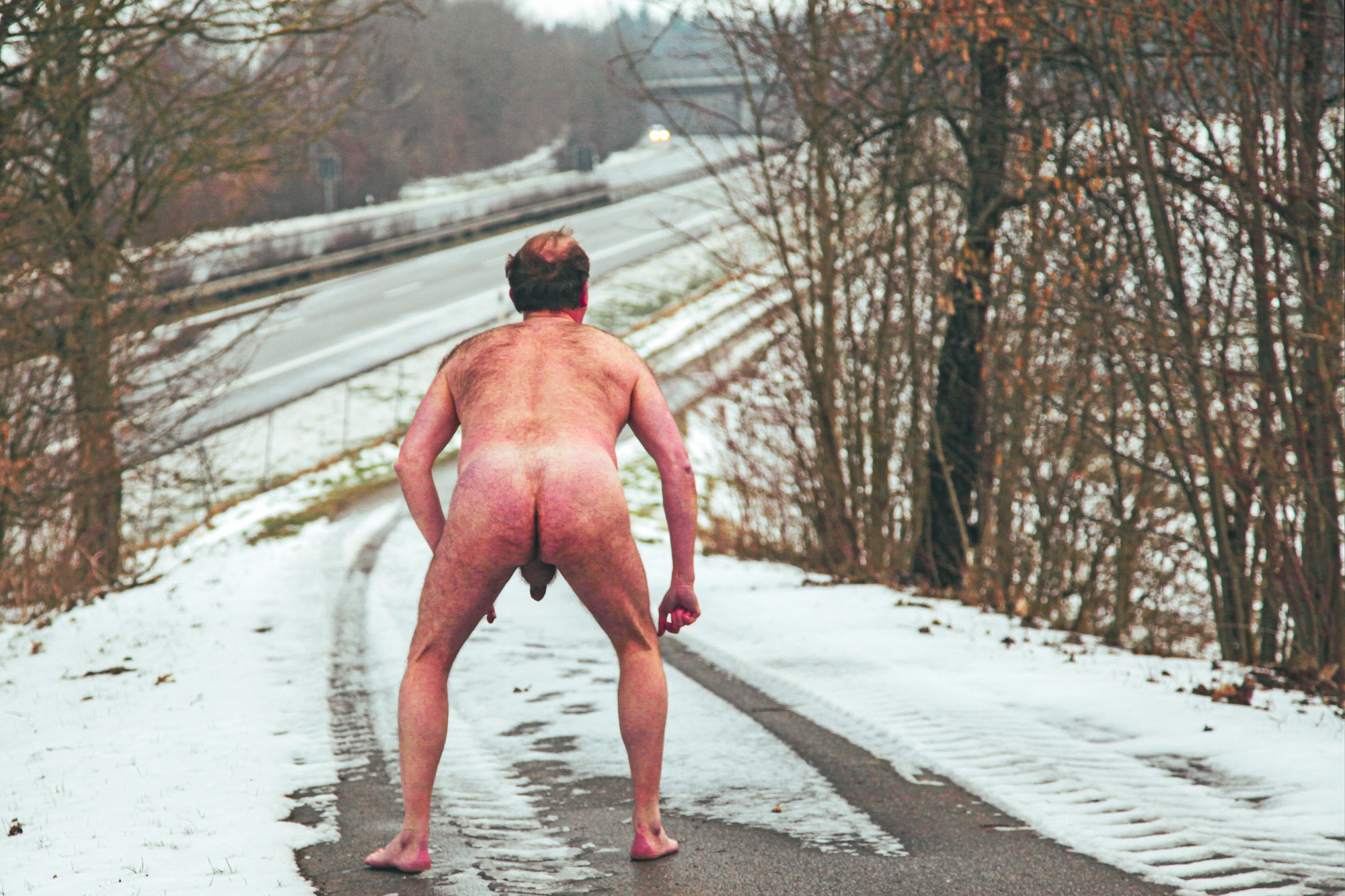 Male nude in the snow next to a highway
