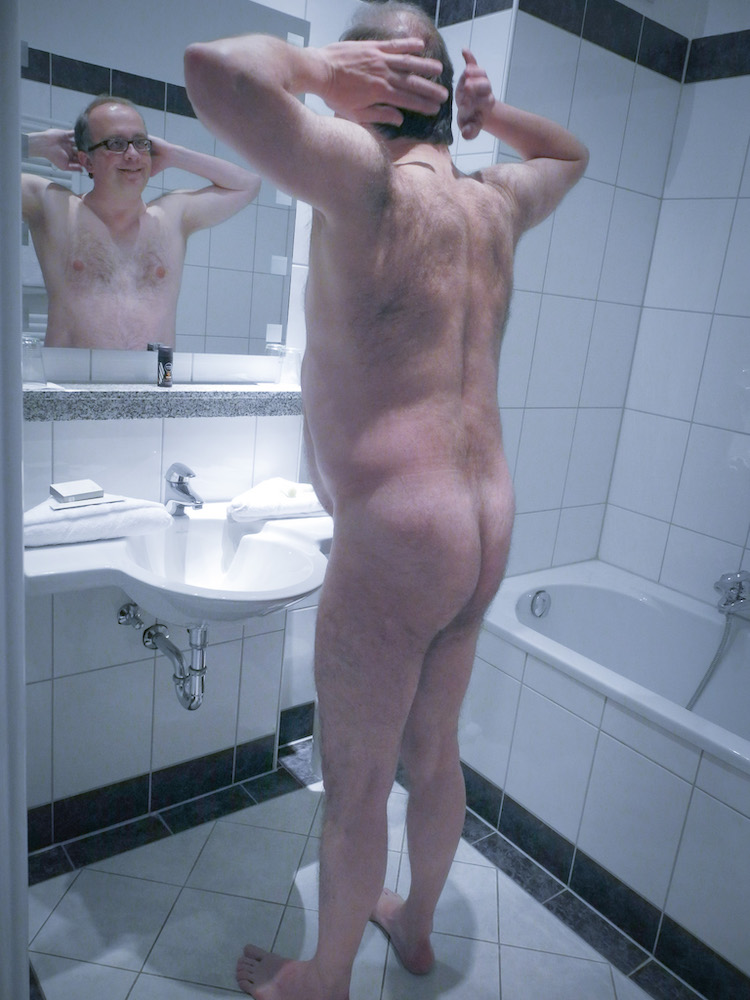 Male nude shows his bum in front of a mirror in a hotel bathroom