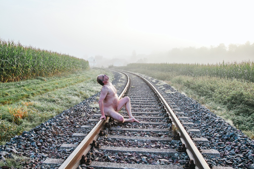 Male nude sitting on railroad track